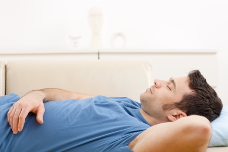 Young man in blue t-shirt sleeping on couch in living room.